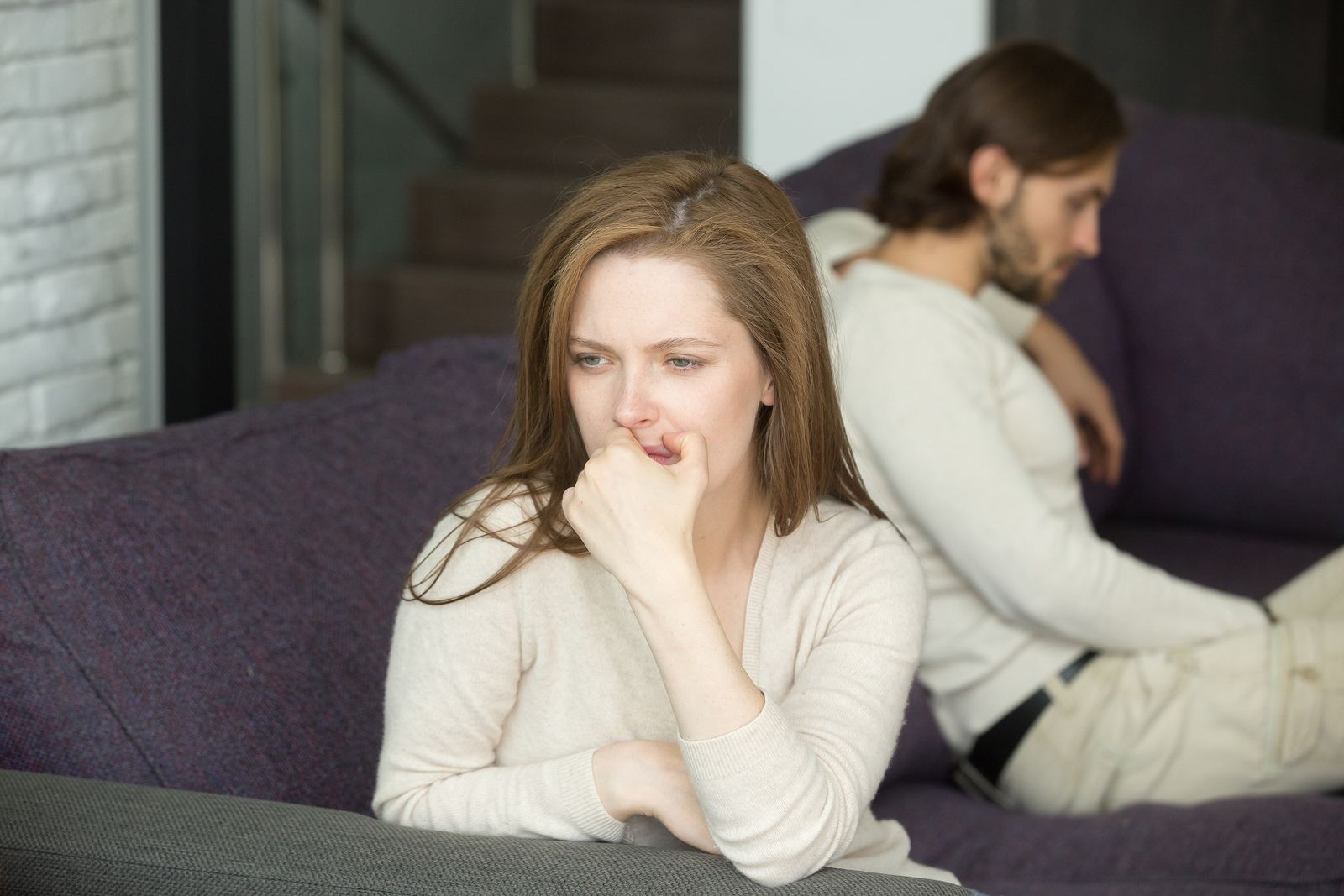 Couple sitting apart after discovering an affair, reflecting on whether to stay or go